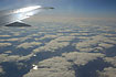 Clouds seen from above with a reflection of the sun in a wing and a water course