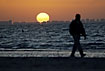 The sun is rising over the city while man is walking along the beach