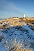 The white light house stands among snow covered dunes this winters morning