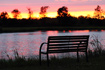 Sunset over pond with an empty bench in the foreground